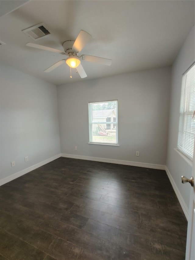 empty room featuring dark wood-type flooring, baseboards, visible vents, and a wealth of natural light