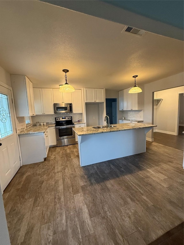 kitchen with stainless steel appliances, white cabinetry, hanging light fixtures, and a center island with sink