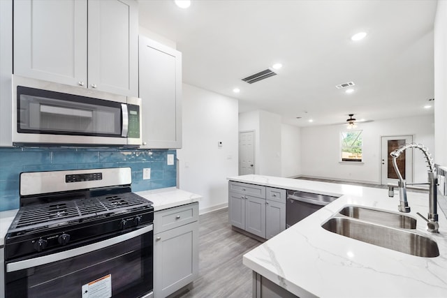 kitchen featuring tasteful backsplash, light hardwood / wood-style flooring, stainless steel appliances, sink, and light stone countertops