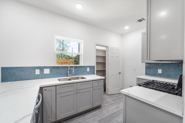 kitchen featuring gray cabinetry, light hardwood / wood-style floors, tasteful backsplash, sink, and light stone counters