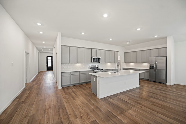 kitchen with dark wood-type flooring, stainless steel appliances, sink, and a kitchen island with sink