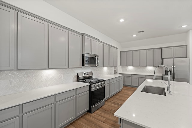 kitchen with tasteful backsplash, dark wood-type flooring, stainless steel appliances, sink, and gray cabinets