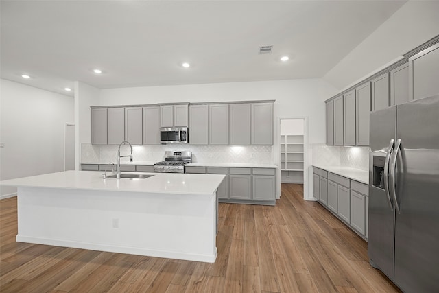 kitchen featuring gray cabinetry, appliances with stainless steel finishes, a kitchen island with sink, sink, and light wood-type flooring