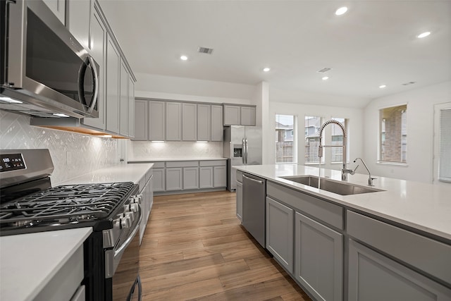 kitchen featuring gray cabinets, stainless steel appliances, sink, decorative backsplash, and light hardwood / wood-style floors