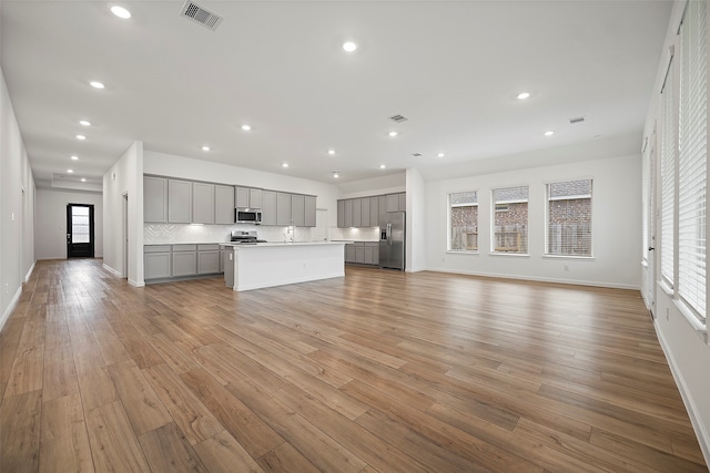 unfurnished living room featuring a healthy amount of sunlight, sink, and light hardwood / wood-style floors