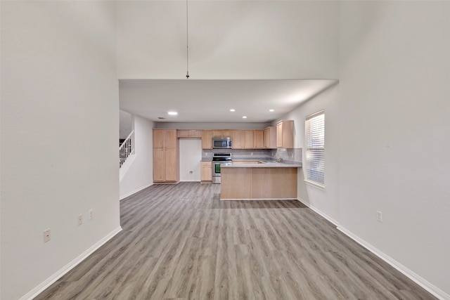 kitchen featuring appliances with stainless steel finishes, hardwood / wood-style flooring, kitchen peninsula, and light brown cabinets