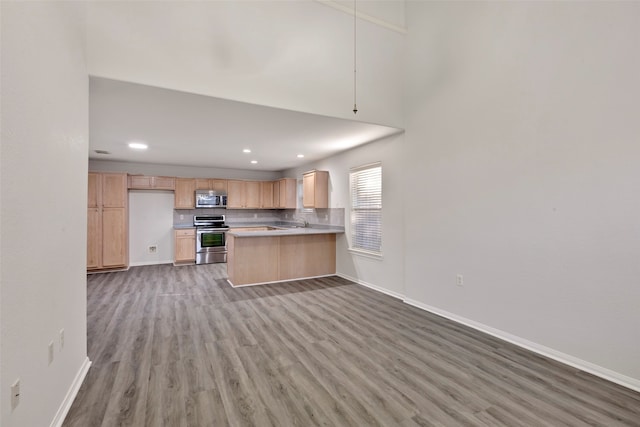 kitchen featuring hardwood / wood-style floors, light brown cabinetry, stainless steel appliances, and kitchen peninsula