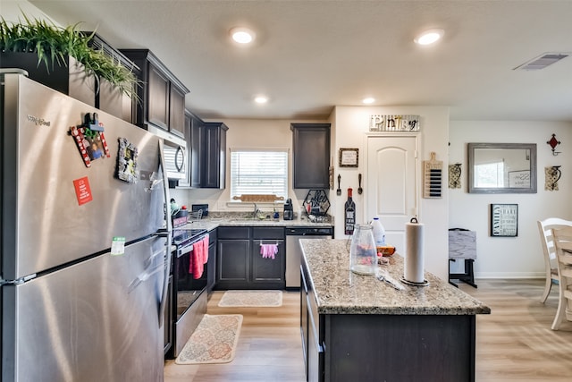 kitchen with a center island, light hardwood / wood-style flooring, light stone counters, and stainless steel appliances