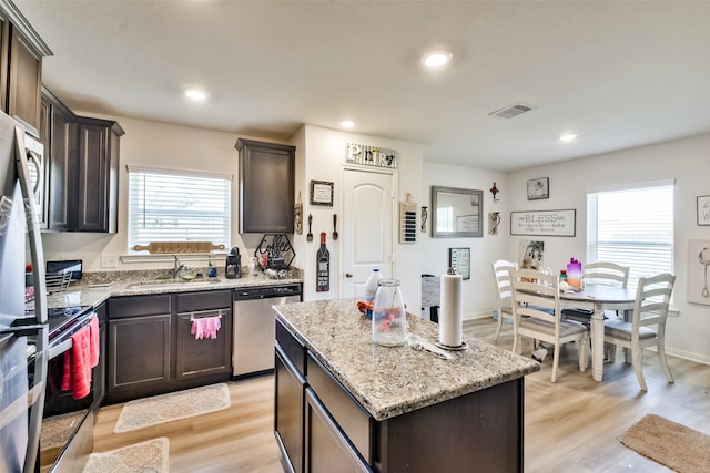 kitchen with light hardwood / wood-style flooring, stainless steel appliances, a center island, light stone countertops, and sink