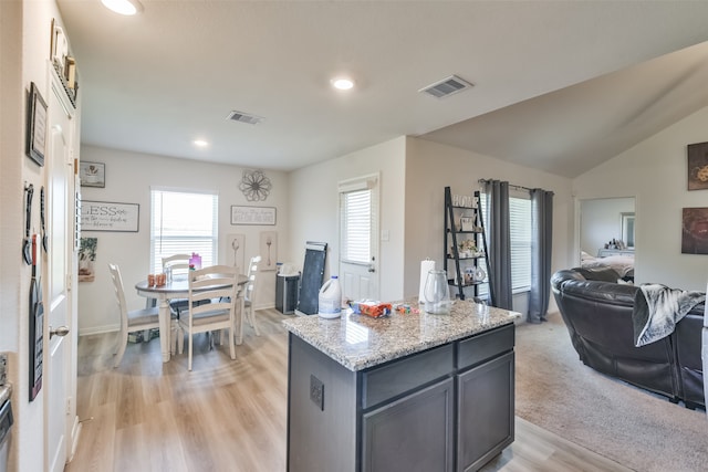 kitchen with light stone countertops, light hardwood / wood-style floors, a center island, gray cabinets, and lofted ceiling