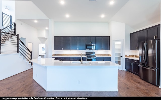 kitchen with high vaulted ceiling, dark hardwood / wood-style flooring, a kitchen island with sink, and appliances with stainless steel finishes