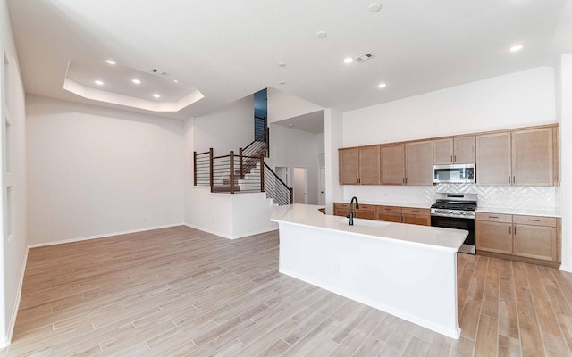 kitchen featuring sink, stainless steel appliances, light hardwood / wood-style floors, and a center island with sink