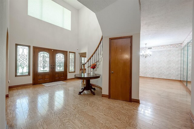 foyer entrance featuring french doors, a high ceiling, a chandelier, light hardwood / wood-style floors, and a textured ceiling