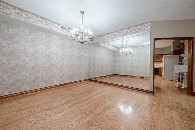 unfurnished dining area featuring a notable chandelier, wood-type flooring, and a textured ceiling