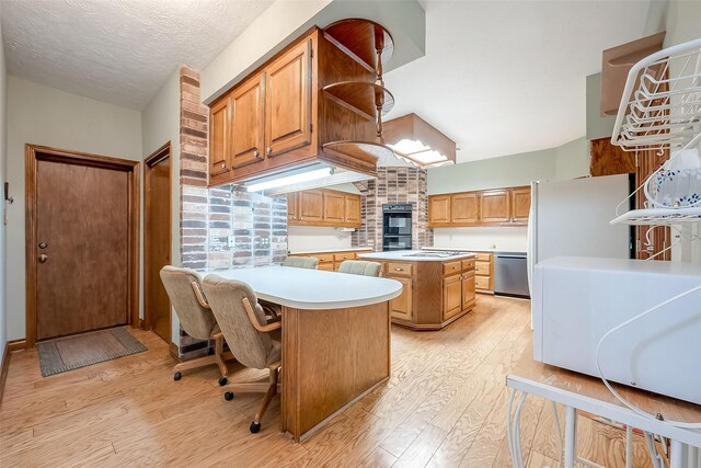 kitchen with stainless steel dishwasher, black double oven, light hardwood / wood-style flooring, a kitchen island, and a breakfast bar area