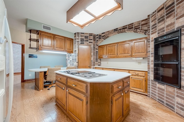 kitchen with stainless steel gas cooktop, light hardwood / wood-style flooring, brick wall, black double oven, and a kitchen island