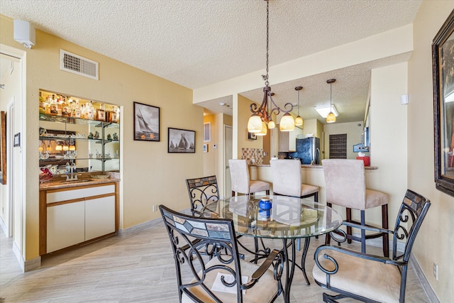 dining space with a textured ceiling, an inviting chandelier, sink, and light hardwood / wood-style floors