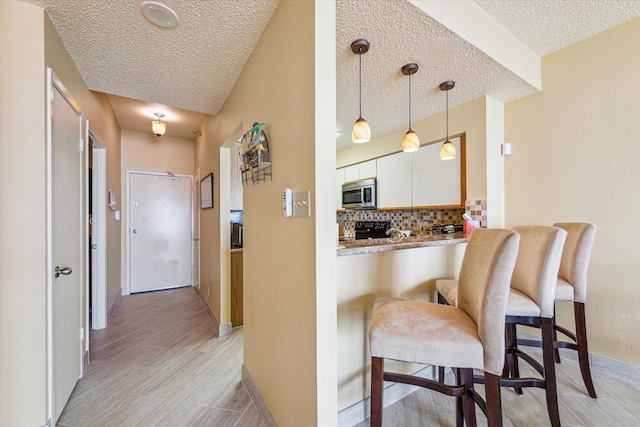 kitchen featuring a textured ceiling, pendant lighting, backsplash, white cabinetry, and light wood-type flooring