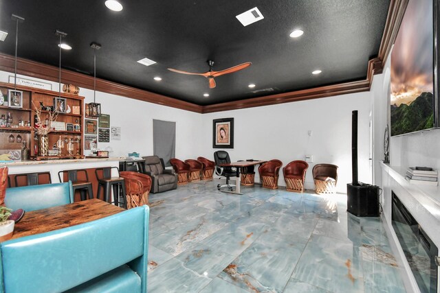 home theater room featuring ceiling fan, indoor bar, a textured ceiling, and ornamental molding