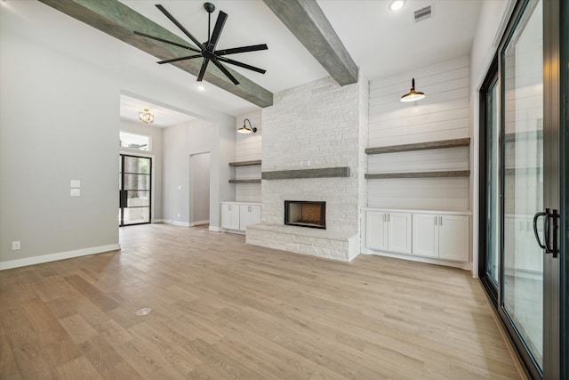 unfurnished living room featuring beam ceiling, a fireplace, light hardwood / wood-style floors, and ceiling fan