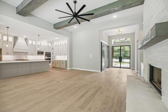 unfurnished living room with beamed ceiling, a brick fireplace, ceiling fan, and light hardwood / wood-style flooring