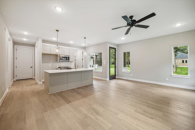 kitchen featuring hanging light fixtures, stainless steel appliances, a wealth of natural light, an island with sink, and white cabinets