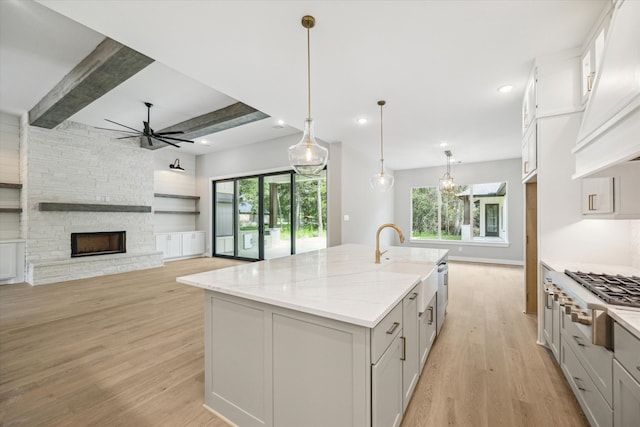 kitchen with light stone counters, hanging light fixtures, appliances with stainless steel finishes, a kitchen island with sink, and white cabinets