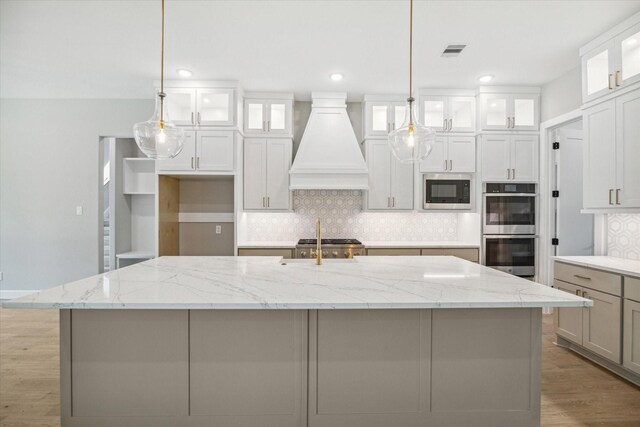 kitchen with a large island, hanging light fixtures, stainless steel double oven, and premium range hood