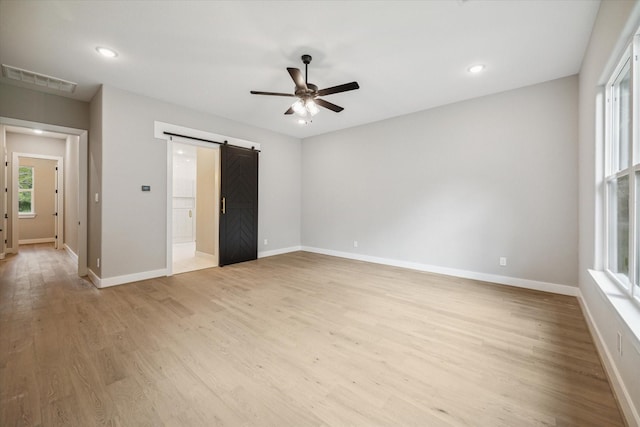 unfurnished bedroom with light hardwood / wood-style floors, a barn door, and ceiling fan