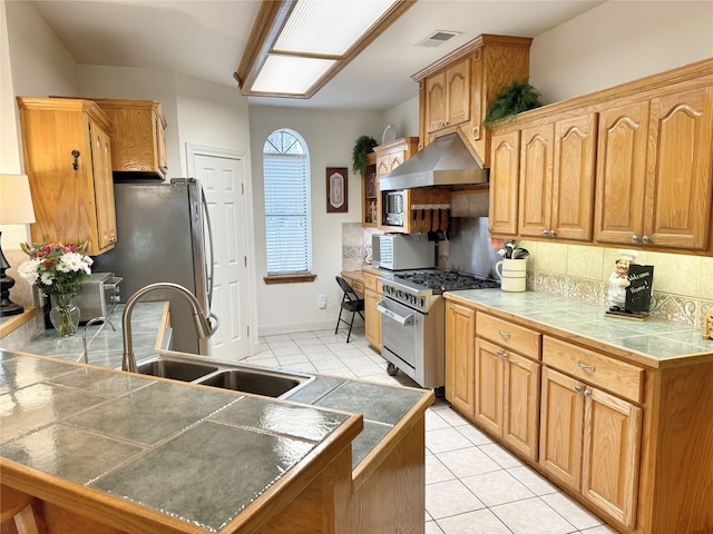 kitchen with tile countertops, exhaust hood, sink, appliances with stainless steel finishes, and light tile patterned flooring