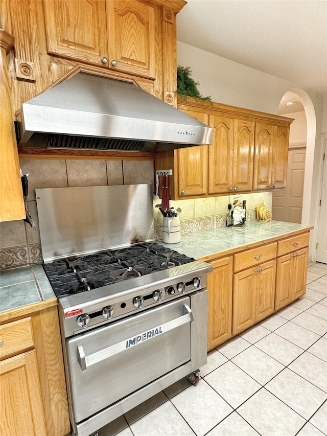 kitchen featuring stainless steel range, tile countertops, tasteful backsplash, ventilation hood, and light tile patterned flooring