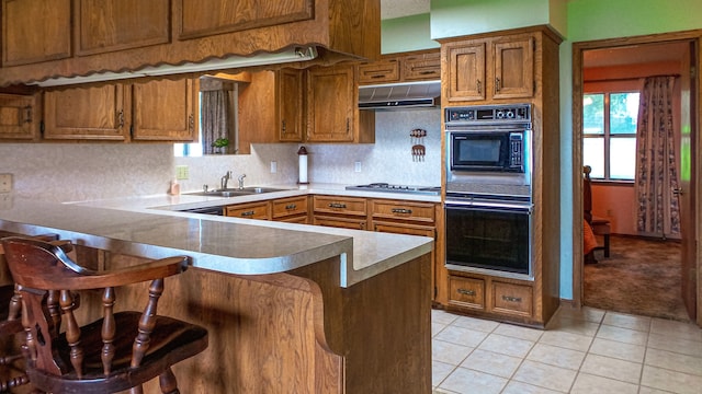 kitchen featuring kitchen peninsula, a kitchen bar, light tile patterned flooring, double oven, and sink