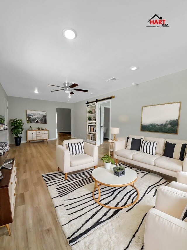 living room with a barn door, ceiling fan, and light hardwood / wood-style flooring