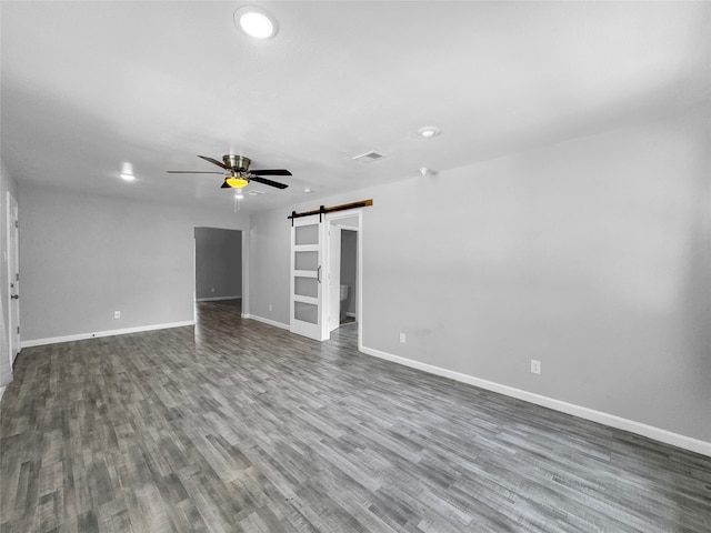 empty room featuring hardwood / wood-style floors, ceiling fan, and a barn door