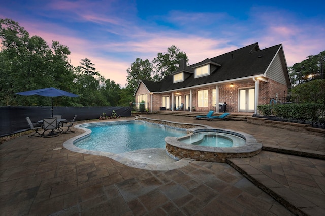 pool at dusk with an in ground hot tub and a patio area