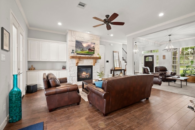 living room featuring a stone fireplace, ornamental molding, ceiling fan with notable chandelier, and dark wood-type flooring