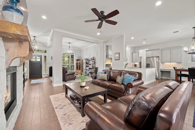 living room with ceiling fan with notable chandelier, ornamental molding, and light hardwood / wood-style flooring