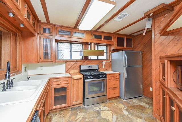 kitchen featuring range hood, beam ceiling, stainless steel appliances, sink, and wooden walls