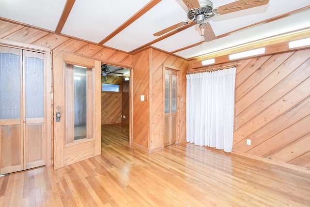 spare room with ceiling fan, wooden walls, and light hardwood / wood-style flooring