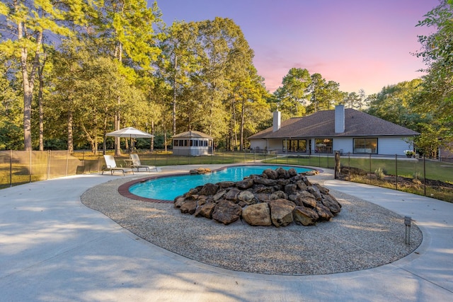 pool at dusk featuring a yard and a patio