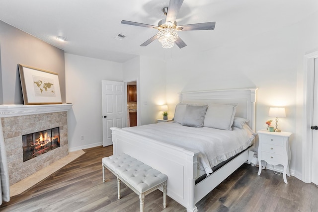 bedroom with dark hardwood / wood-style flooring, ceiling fan, and a tiled fireplace