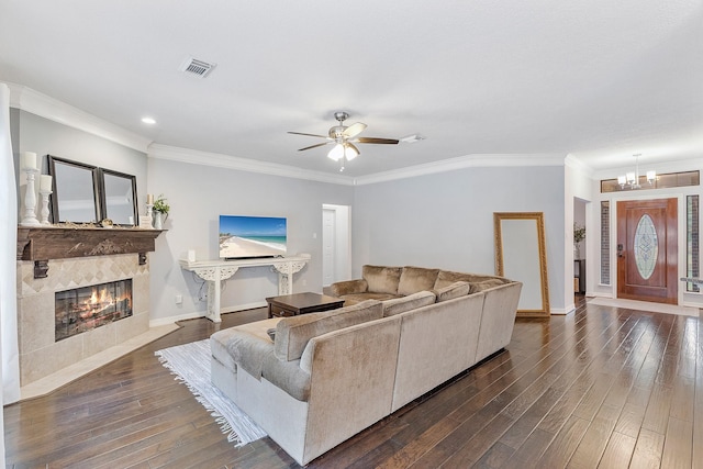 living room with dark hardwood / wood-style flooring, a tiled fireplace, ceiling fan with notable chandelier, and crown molding