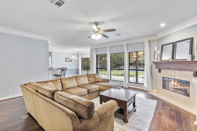 living room featuring hardwood / wood-style floors, ceiling fan with notable chandelier, ornamental molding, a fireplace, and a textured ceiling