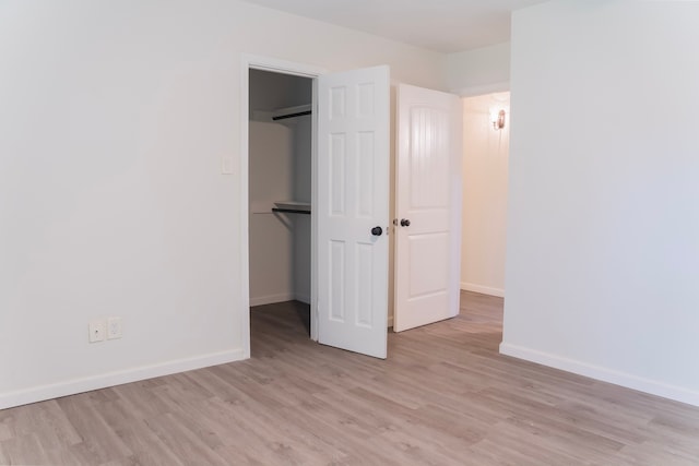 unfurnished bedroom featuring a closet, a walk in closet, and light hardwood / wood-style floors