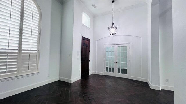 foyer entrance featuring an inviting chandelier, crown molding, french doors, a high ceiling, and dark parquet flooring