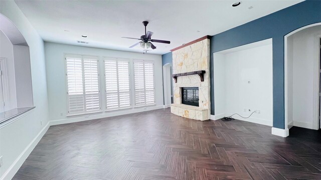 unfurnished living room with a fireplace, dark parquet flooring, and ceiling fan