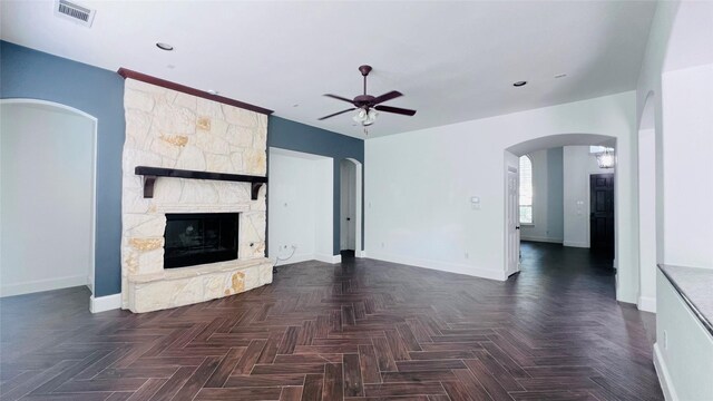 unfurnished living room featuring dark parquet flooring, ceiling fan, and a fireplace