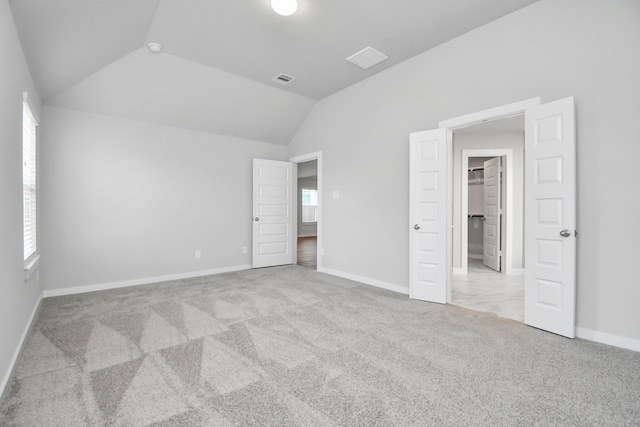 unfurnished bedroom featuring a closet, vaulted ceiling, a walk in closet, and light carpet