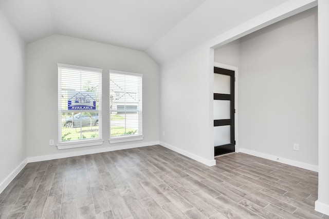 spare room featuring light wood-type flooring and vaulted ceiling