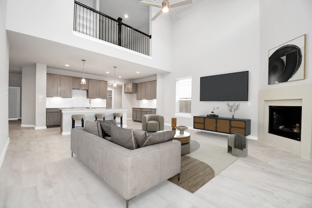 living room with a high ceiling, ceiling fan, and light hardwood / wood-style floors